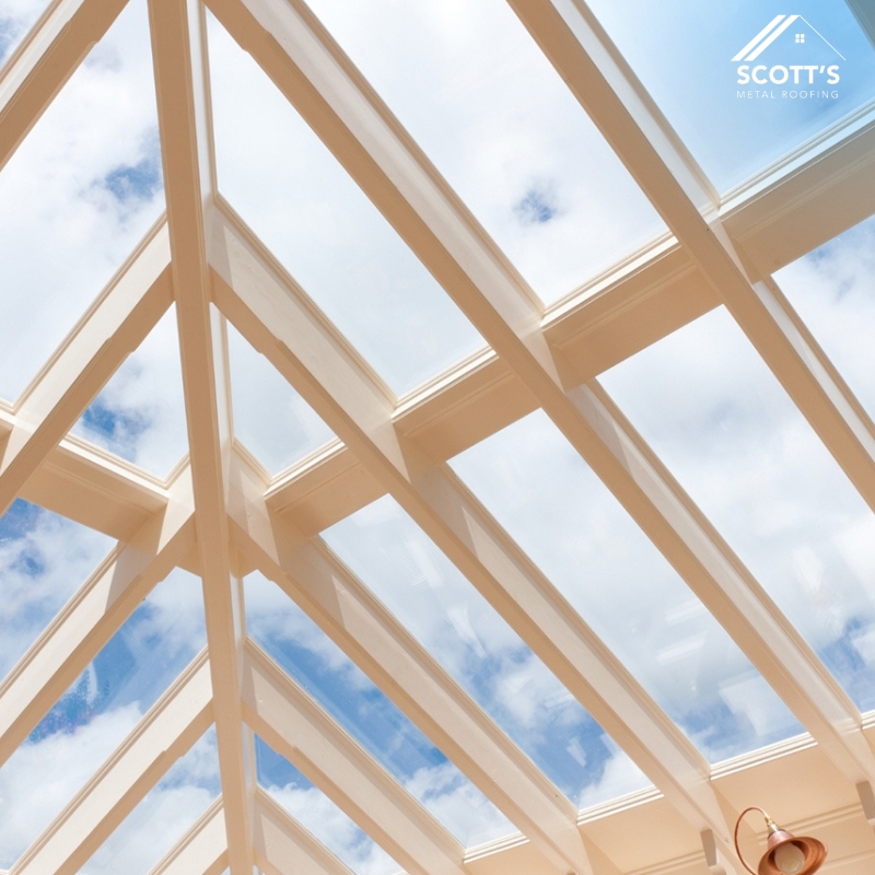 Metal Roof Skylight Installation with clear glass panels, white framing, and blue sky reflection, enhancing natural light indoors.