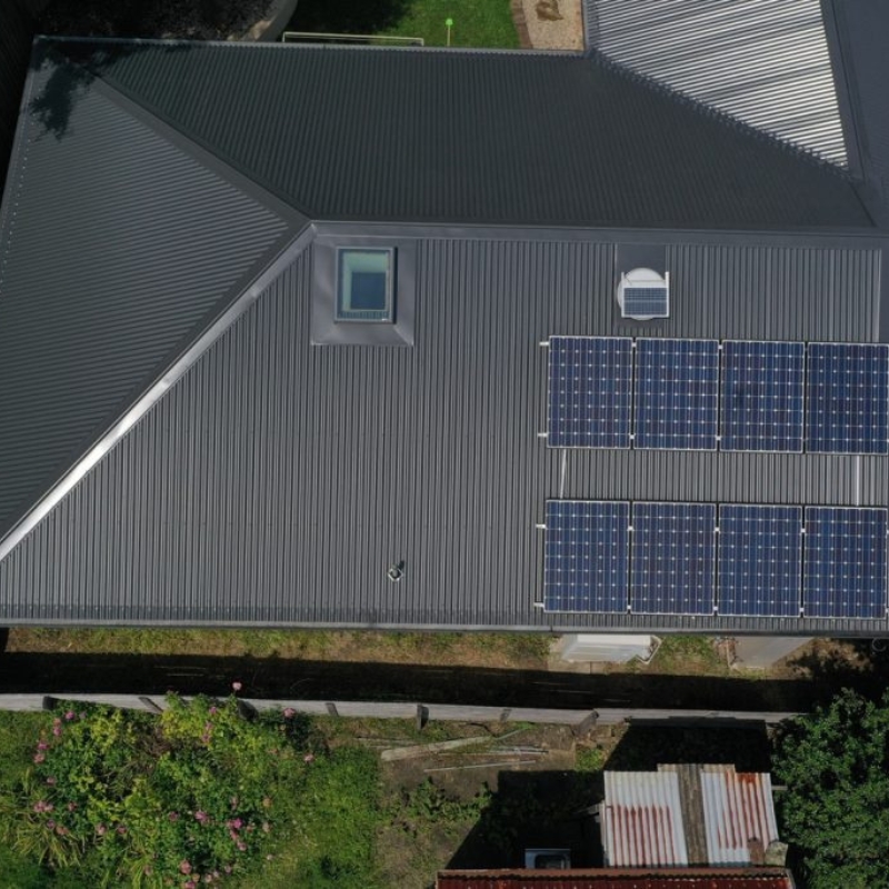 A house with a metal roof extension, solar panels, and skylight, showcasing energy efficiency and contemporary roofing solutions.