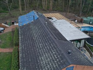 House with active metal roof leaks, showing blue tarp and timber frame repairs.