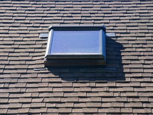 A skylight is centrally placed on a brown shingle roof, showcasing typical skylight placement.