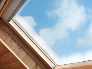 Clear blue sky visible through timber-framed skylight, showing benefits of adding a skylight to indoor spaces.