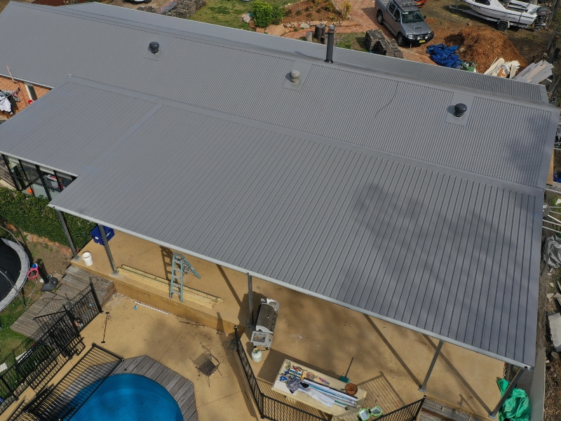 House with a metal roof featuring covered patio and backyard pool area, viewed from above