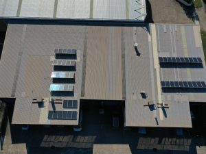 Commercial roofing materials with solar panels installed on a large industrial metal roof viewed from above