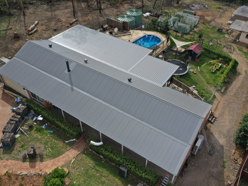 Aerial view of house with a metal roof, garden, water tanks, and outdoor play area