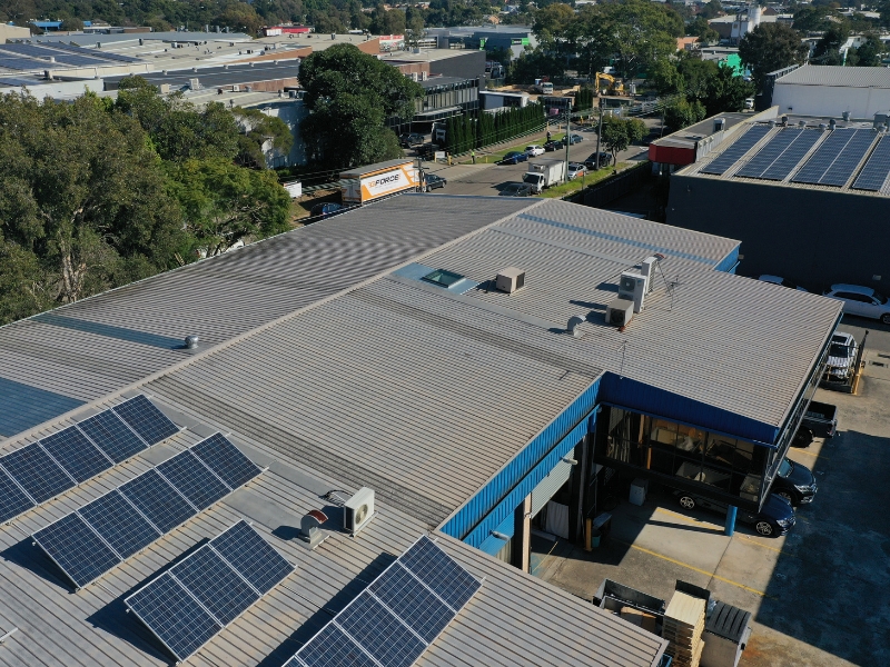 Metal commercial roofing materials on warehouse with solar panels and ventilation units in suburban business district