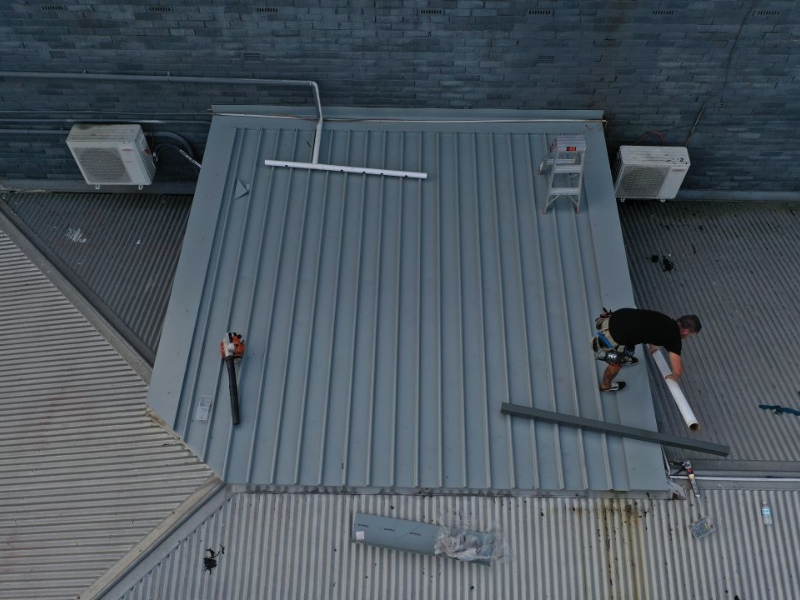 Metal roof installation guide showing contractor fitting piping on ribbed metal roofing.